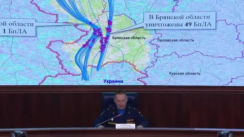 Russian Defence Ministry A Russian defence ministry official sits in front of a large screen which shows a map, marked with the the alleged flight paths of the drones Russia says Ukraine launched at one of Putin's residences.